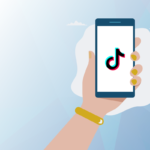 Graphic on standard seoplus+ blue triangle background, with illustration of a hand holding a mobile phone with the TikTok logo in the centre.